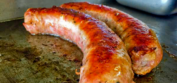 Sausages from Beez Neez cooking on a flattop grill.