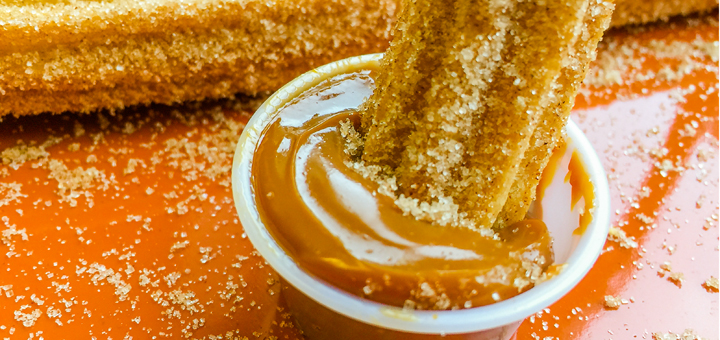 the churros locos dulce de leche dipping sauce with a churro stuck in it