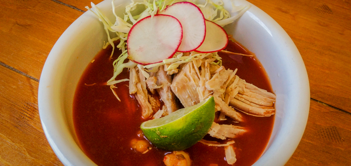 A photo of a white bowl filled with pozole, pork shoulder, shredded cabbage, radishes, and a slice of lime. The pozole comes from Pozole To The People. One of the food products developed through the Getting Your Recipe To Market program from the Portland Community College Small Business Development Center.